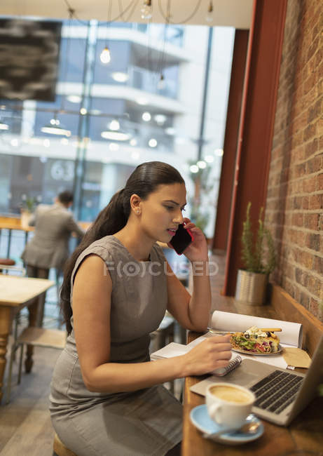 Businesswoman talking on smart phone, working at laptop in cafe — Stock Photo