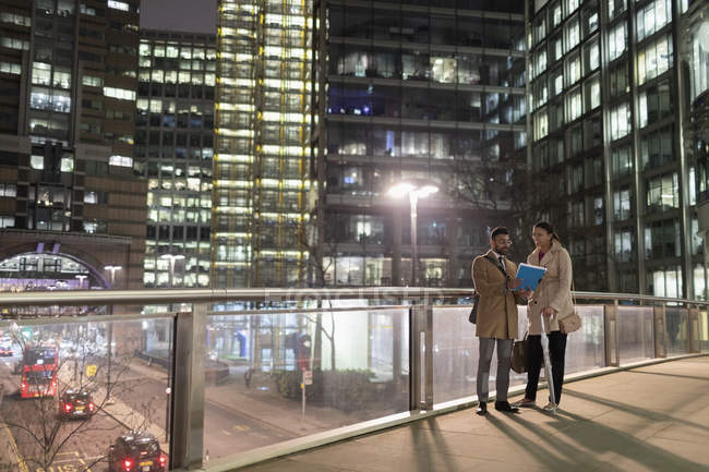 Gente de negocios discutiendo papeleo en puente peatonal urbano por la noche - foto de stock
