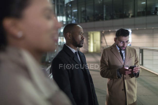 Uomo d'affari che utilizza lo smart phone sul ponte pedonale urbano di notte — Foto stock