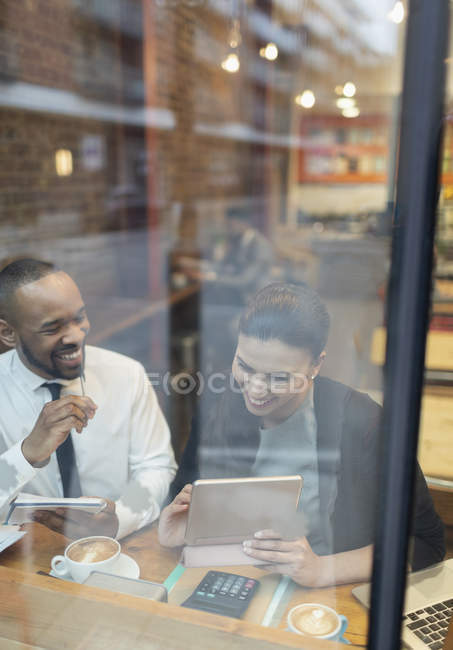 Улыбающиеся бизнесмены с помощью цифрового планшета, работающие у окна кафе — стоковое фото