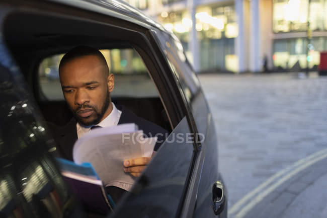 Businessman reading paperwork in crowdsourced taxi at night — Stock Photo