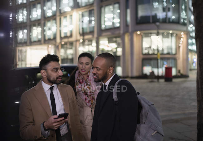 Pessoas de negócios com telefone inteligente falando na rua da cidade à noite — Fotografia de Stock