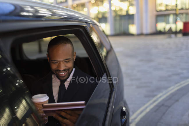Бизнесмен пьет кофе и пользуется цифровым планшетом в такси — стоковое фото