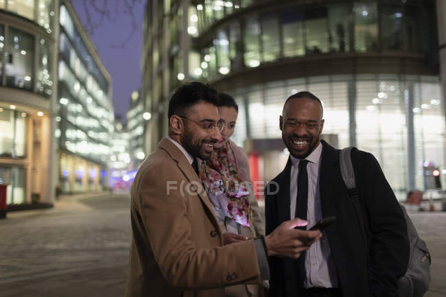 Business people using smart phone on urban street at night — Stock Photo