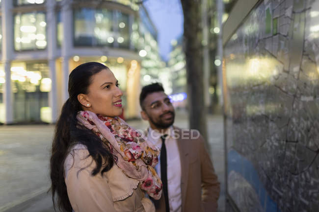 Business people looking at city map on urban street at night — Stock Photo