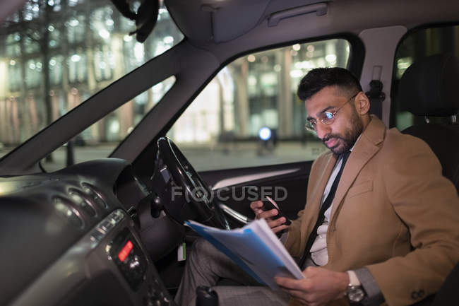 Бізнесмен зі смартфоном читає документи в машині вночі — стокове фото