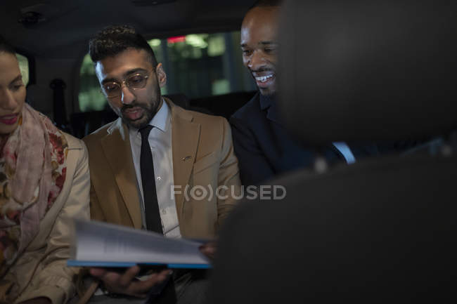 Ділові люди обговорюють документи на задньому сидінні краудсорсингового таксі — стокове фото