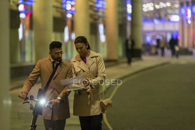 Business people with bicycle and paperwork walking on urban street at night — Stock Photo