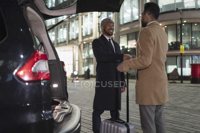 Geschäftsleute mit Koffer beim nächtlichen Händeschütteln im Auto auf der Stadtstraße — Stockfoto