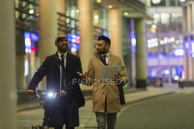 Businessmen talking, discussing paperwork on urban sidewalk at night — Stock Photo