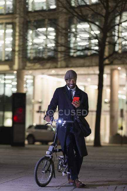 Homme d'affaires avec vélo utilisant un téléphone intelligent sur le trottoir urbain la nuit — Photo de stock