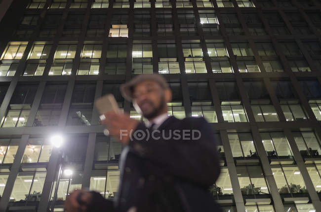 Businessman using smart phone below urban highrise at night — Stock Photo