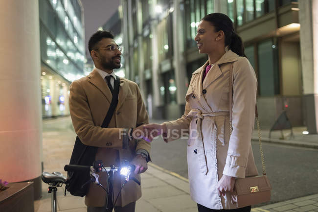 Business people with bicycle handshaking on urban sidewalk at night — Stock Photo