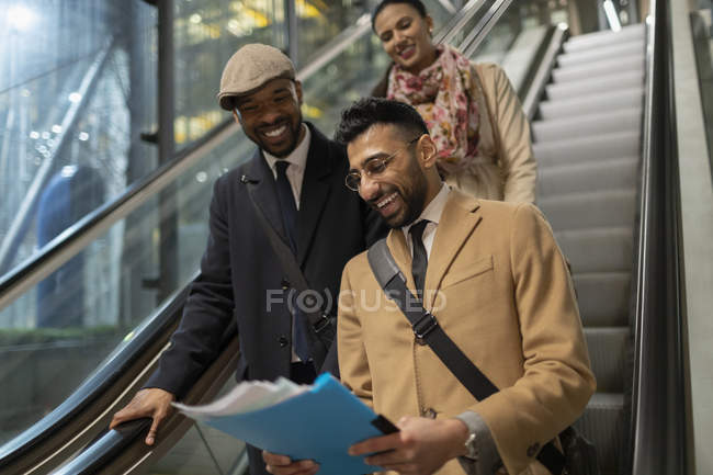 Gente de negocios sonriente leyendo papeleo sobre escaleras mecánicas - foto de stock