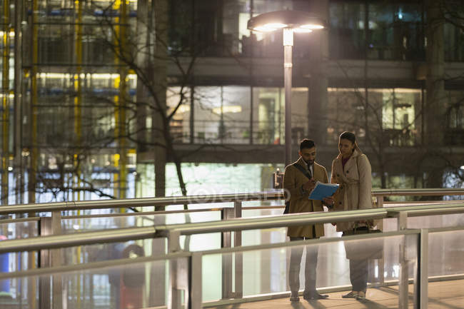 Empresários discutindo papelada sobre ponte pedonal urbana à noite — Fotografia de Stock