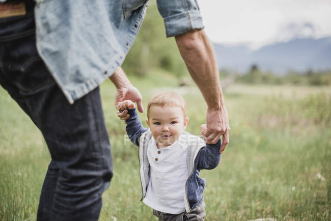 Pai andando com o bebê filho no campo gramado — Fotografia de Stock