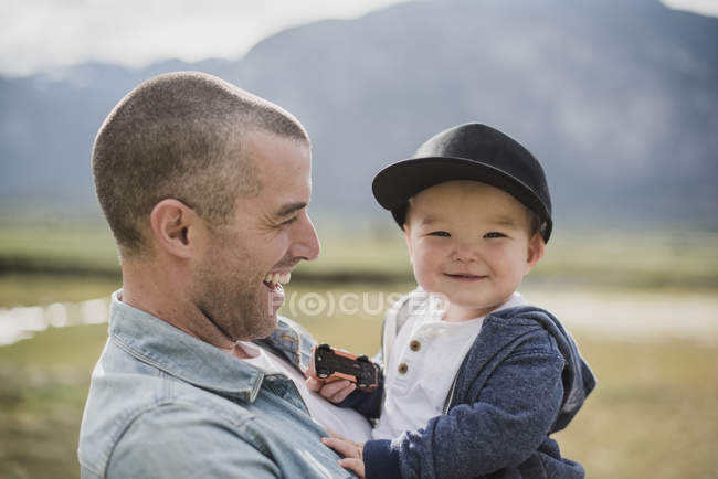 Padre sosteniendo lindo, feliz bebé hijo mirando a la cámara - foto de stock
