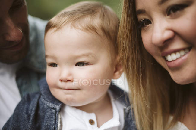 De cerca sonriendo padres y lindo bebé hijo mirando hacia otro lado - foto de stock