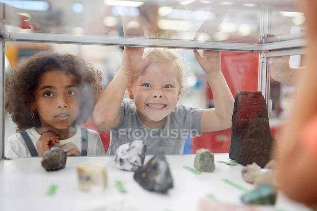 Chica tonta haciendo una cara en la vitrina de exhibición de roca en el centro de ciencia - foto de stock