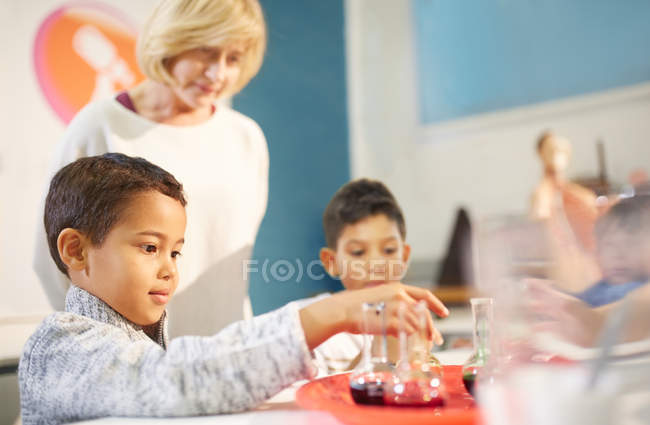 Teacher watching curious students playing with beakers at interactive exhibit in science center — Stock Photo