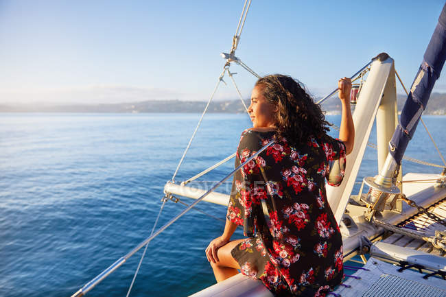 Serene young woman relaxing on sunny catamaran, looking out at blue ocean — Stock Photo