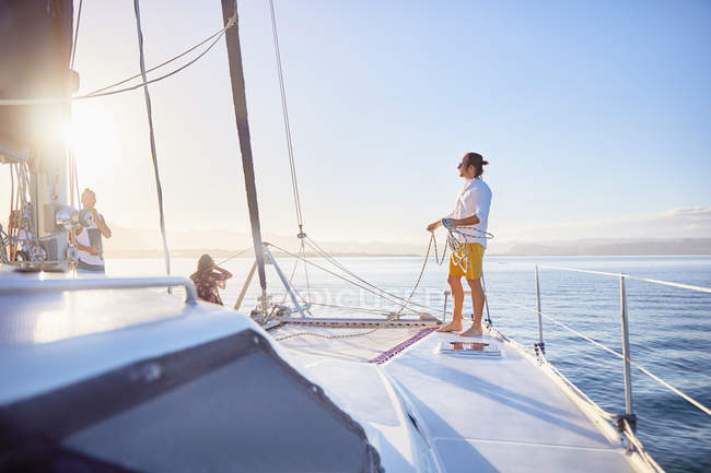 Giovane uomo che tiene la corda di sartiame sul catamarano soleggiato — Foto stock