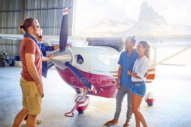 Friends talking at prop airplane in airplane hangar — Stock Photo