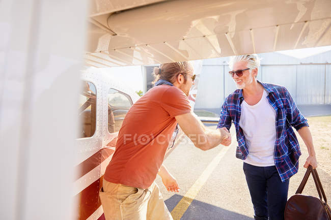 Piloto estrechando la mano con el hombre abordando pequeño avión - foto de stock