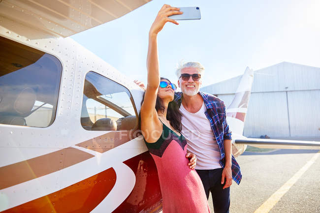 Couple taking selfie with camera phone at small airplane — Stock Photo