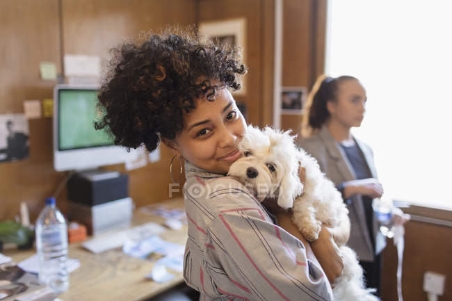Retrato sonriente mujer de negocios creativa con lindo perro en la oficina - foto de stock