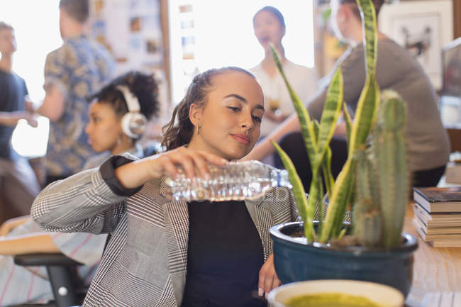Businesswoman watering cactus plant with bottle water in office — Stock Photo