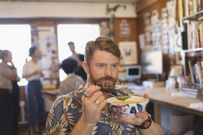 Creative businessman eating soup in office — Stock Photo