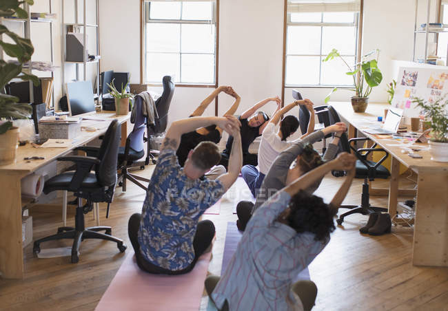 Creative business people stretching, practicing yoga in office — Stock Photo