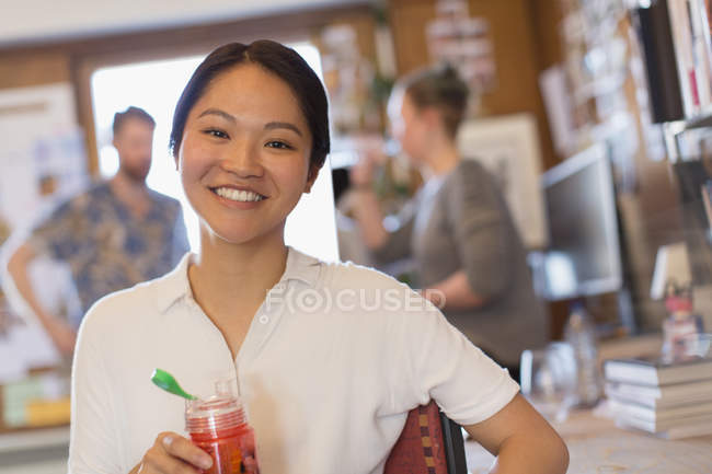 Портрет улыбающейся творческой предпринимательницы, пьющей сок в офисе — стоковое фото