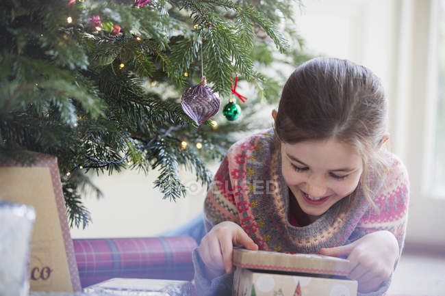 Sonriente, chica curiosa abriendo regalo de Navidad - foto de stock
