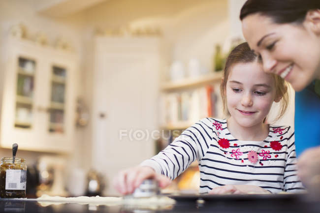 Mother and daughter baking, using cookie cutter in kitchen — Stock Photo