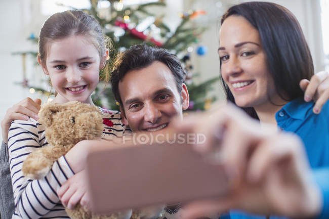Familia feliz con teléfono inteligente tomando selfie en la sala de estar de Navidad - foto de stock
