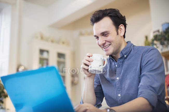 Uomo sorridente che beve caffè, lavora al computer portatile — Foto stock
