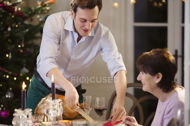Сын подает рождественскую индейку старшей матери за обеденным столом при свечах — стоковое фото