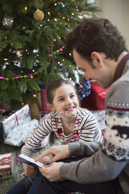 Padre leyendo el libro con su hija en el árbol de Navidad - foto de stock