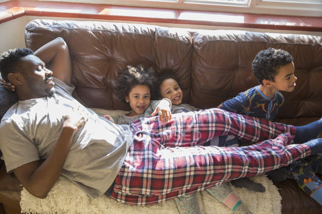 Portrait happy, carefree kids in pajamas cuddling with father on living room sofa — Stock Photo