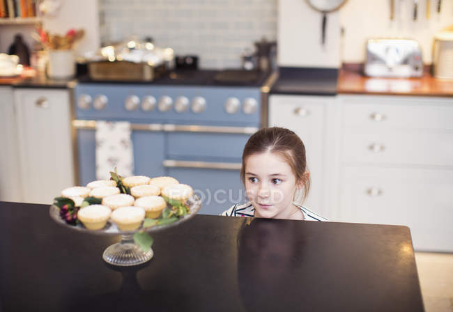 Cute girl eyeing Christmas pies on kitchen counter — Stock Photo