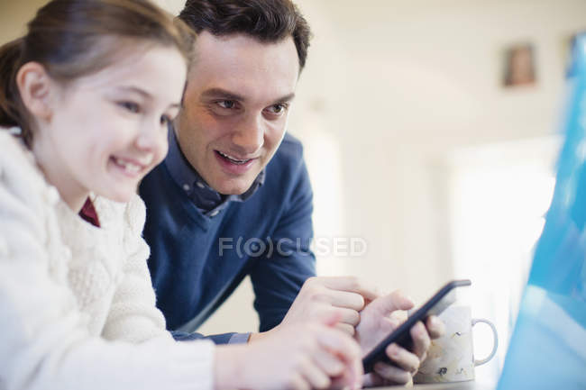 Отец со смартфоном с помощью ноутбука с дочерью — стоковое фото