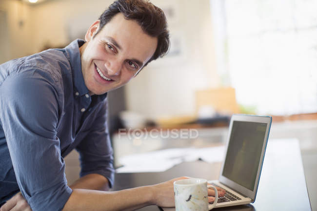 Homme souriant et confiant travaillant à l'ordinateur portable dans la cuisine — Photo de stock