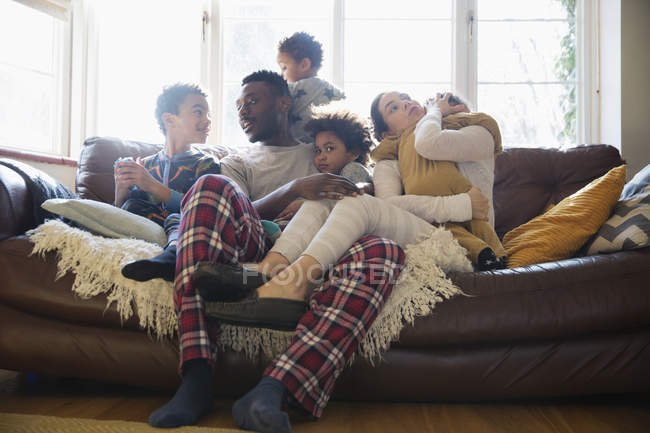 Молодая семья отдыхает в пижаме на диване в гостиной — стоковое фото
