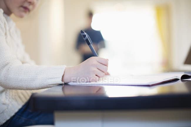 Дівчина з ручкою і робочою книгою робить домашнє завдання за столом — стокове фото