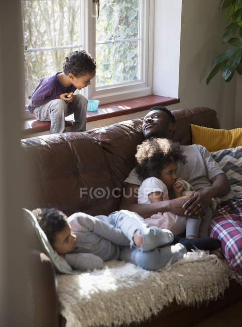 Отец и дети отдыхают, обнимаются на диване в гостиной — стоковое фото