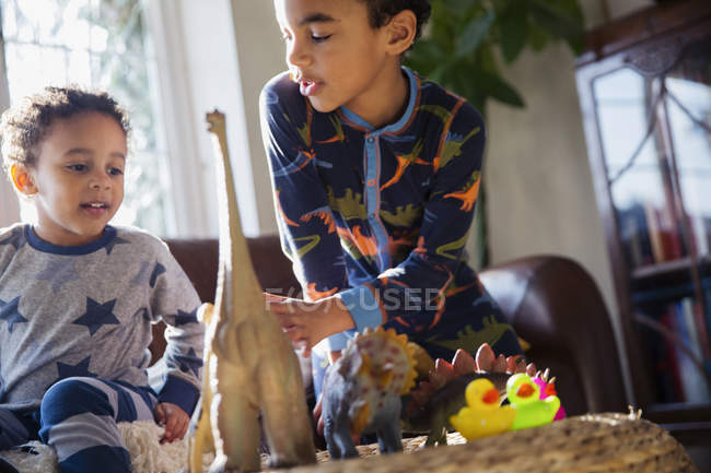 Hermanos en pijama jugando con juguetes de dinosaurios - foto de stock