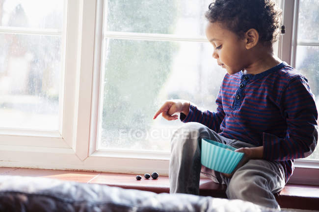 Niedlicher, unschuldiger Junge beim Zählen von Snacks auf der Fensterbank — Stockfoto