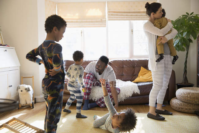 Багатоетнічна молода сім'я в піжамі грає і розслабляється у вітальні — стокове фото